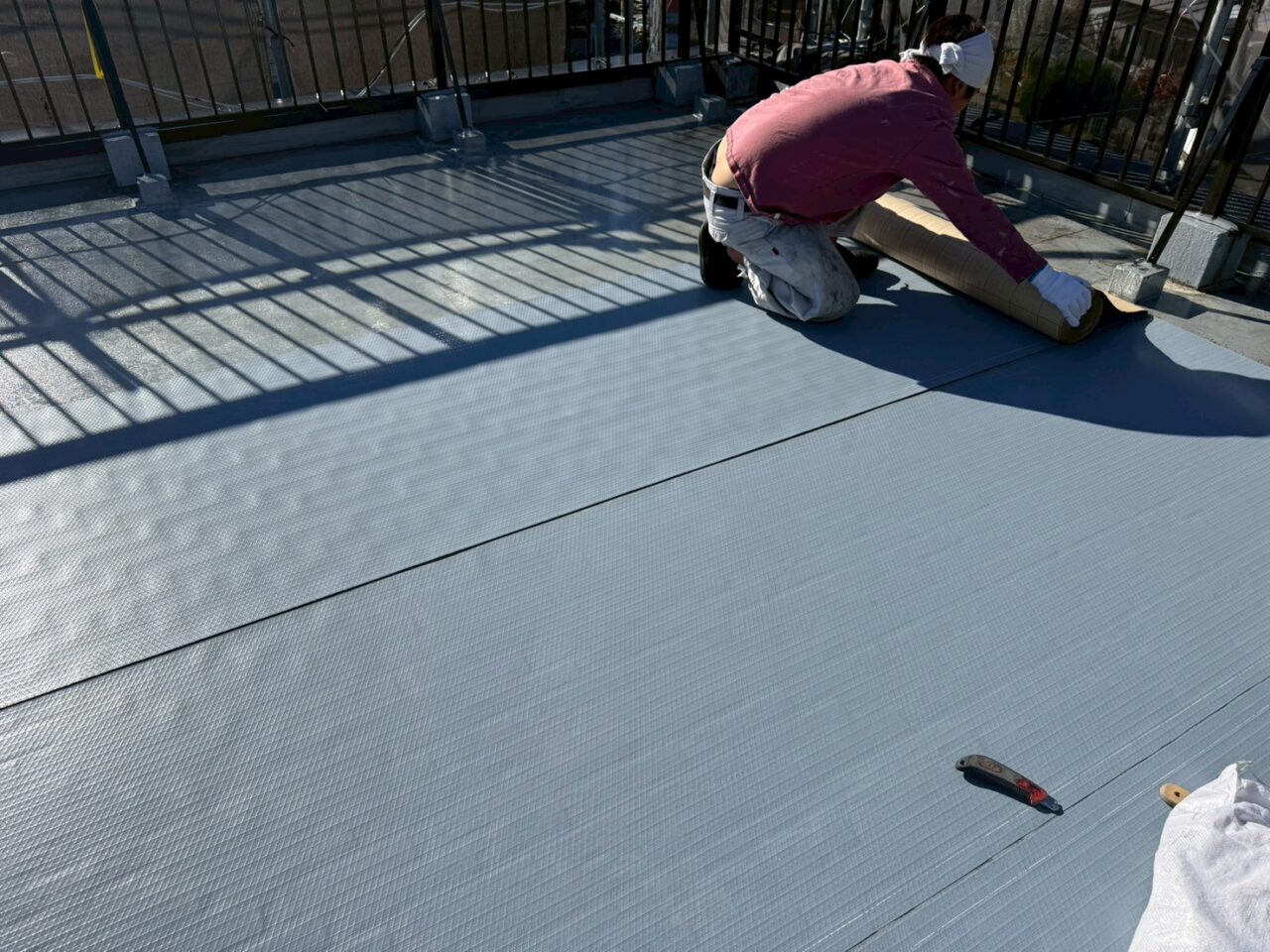 通気緩衝シートを屋上に貼り付けている作業中の様子