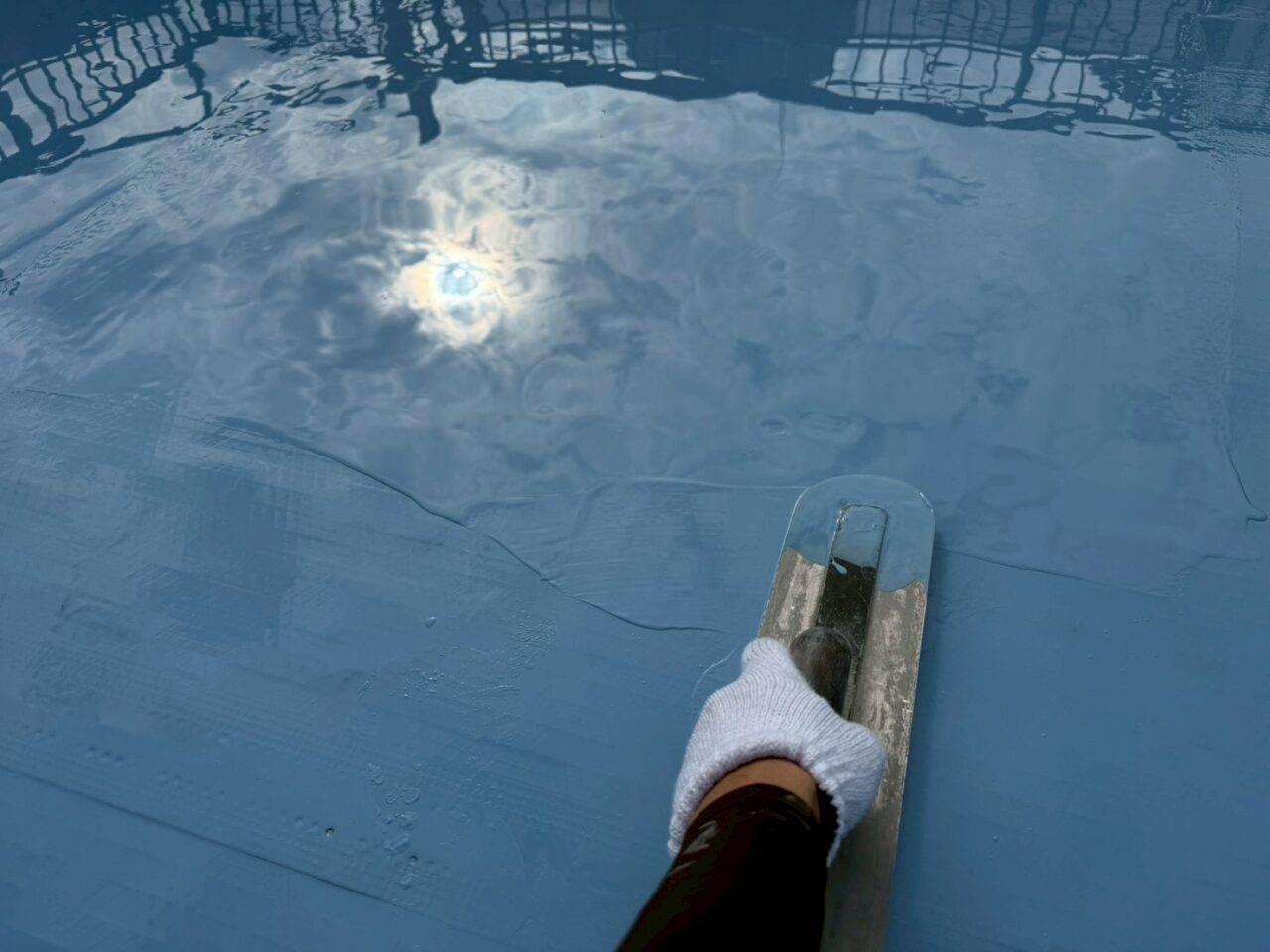 ウレタン防水材を塗布中の作業手元、ローラーで丁寧に均している様子（池田市屋上防水工事）